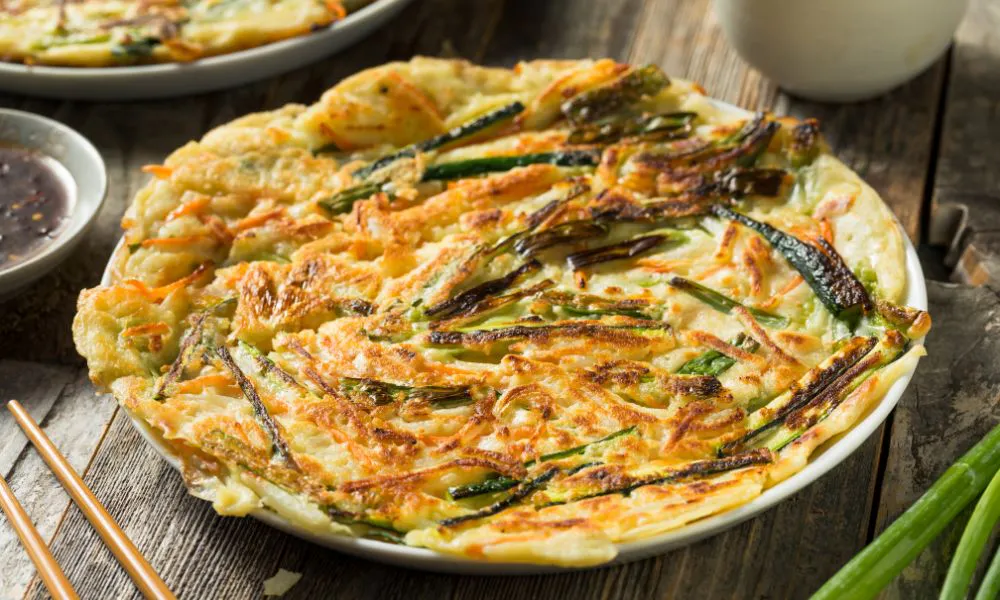 Golden crispy Korean scallion vegetable pancake served on white plate with dark dipping sauce at Eat Time, a Chinese Restaurant in Burien