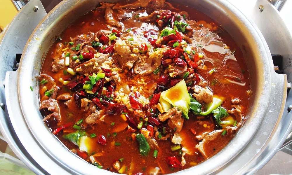 Spicy boiled beef in vibrant red chili broth topped with dried chilies, garlic, green onions and leafy greens at Eat Time, a Chinese Restaurant in Burien